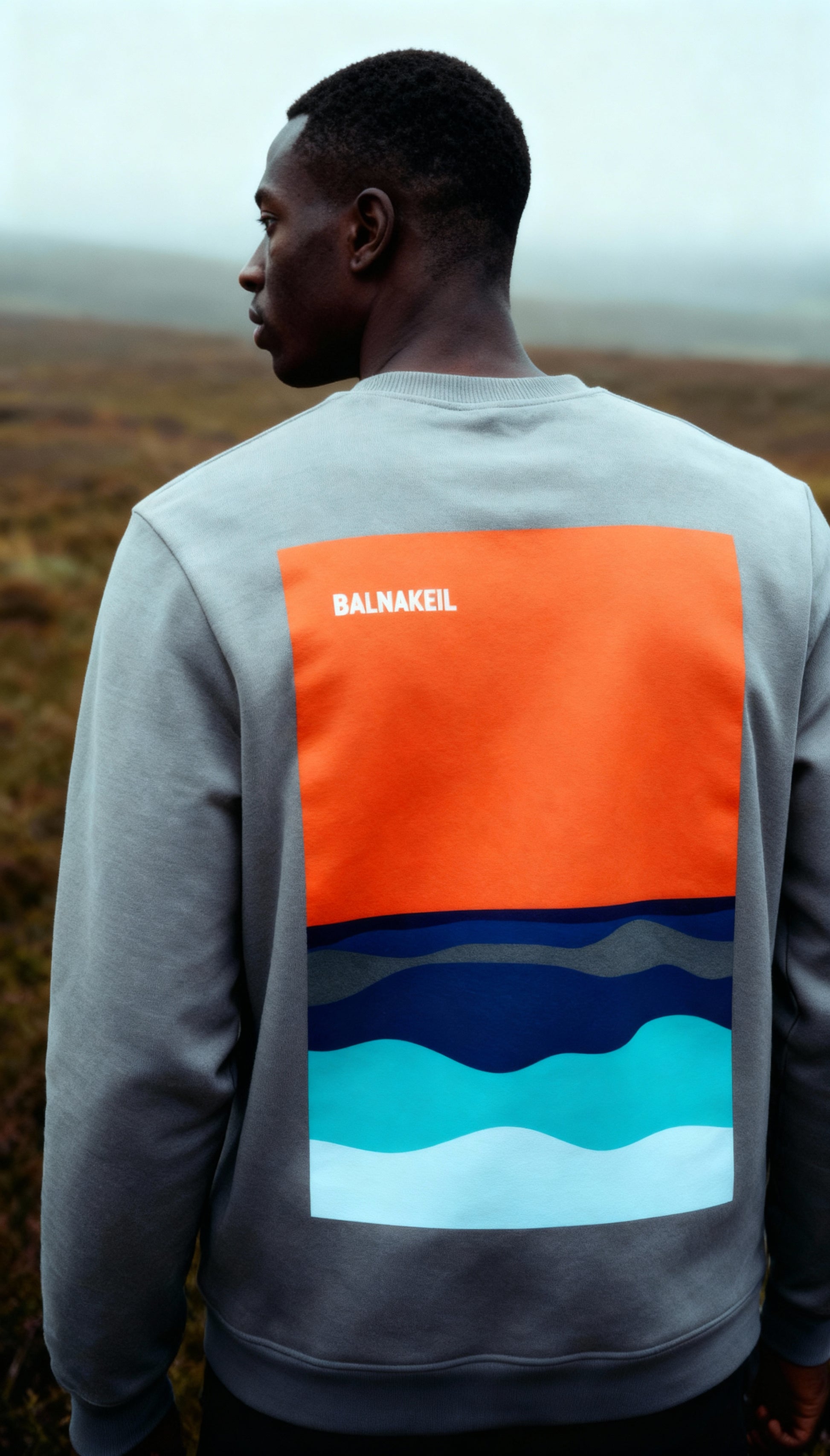 Person wearing a sweatshirt with an orange, blue, and white design on the back, standing outdoors.