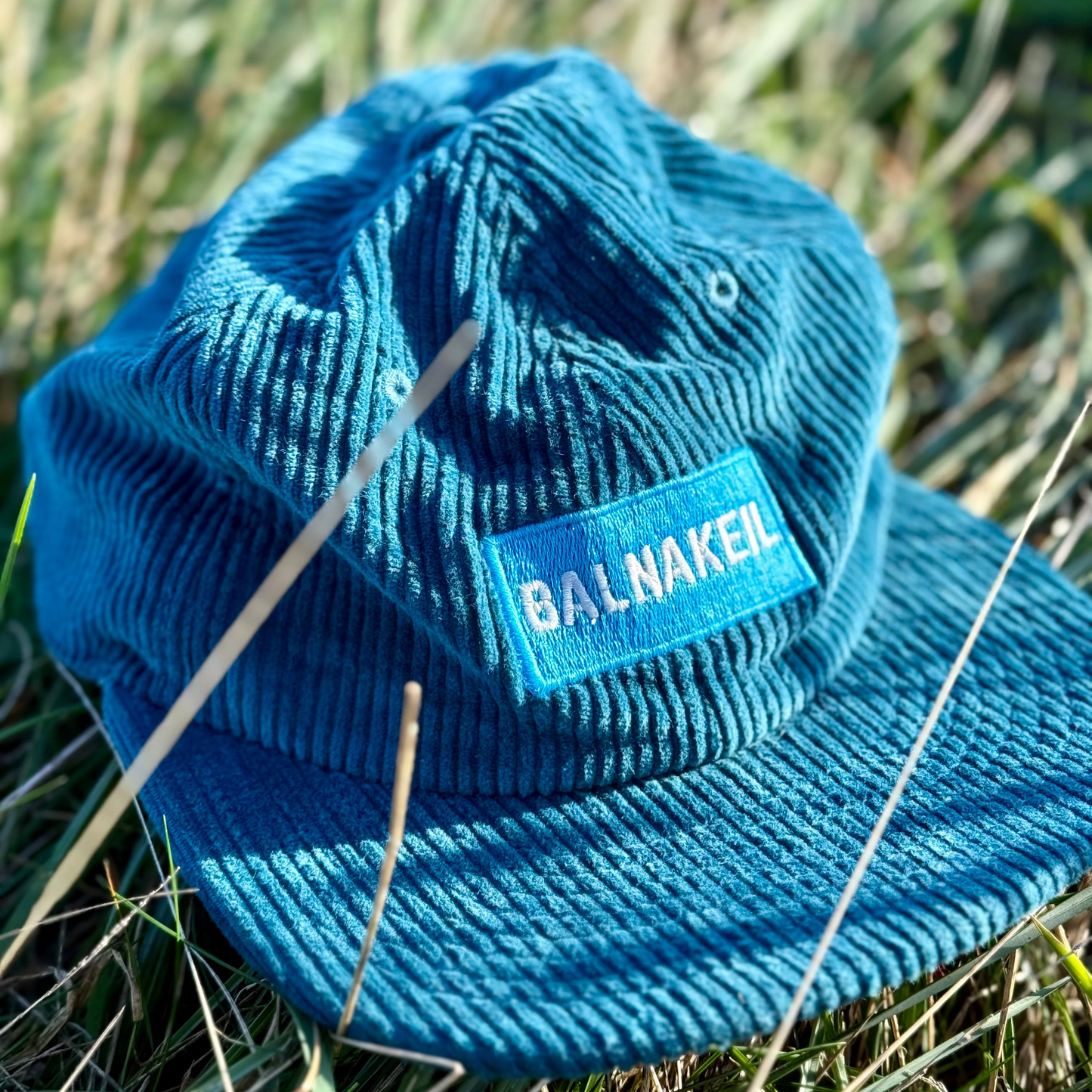 Blue cord cap with 'Balnakeil' label on grass