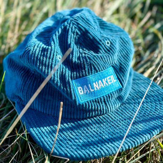 Blue cord cap with 'Balnakeil' label on grass