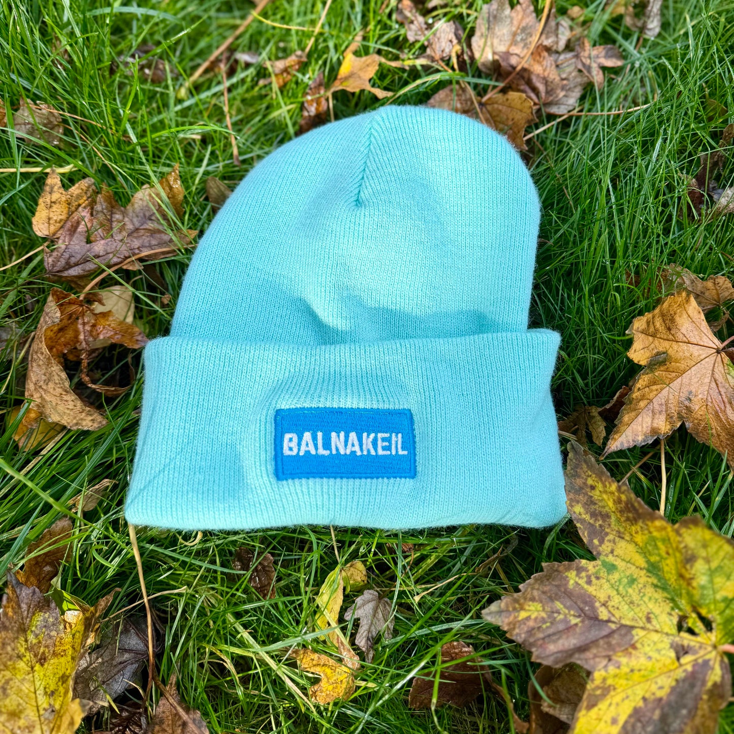 Light blue beanie with a brand logo on grass and leaves