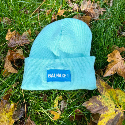 Light blue beanie with a brand logo on grass and leaves