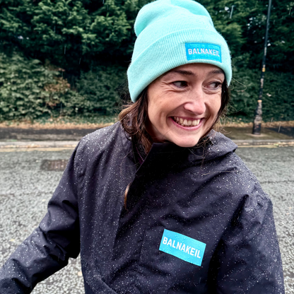 Person wearing a dark jacket and light blue beanie with 'Balnakeil' branding outdoors.