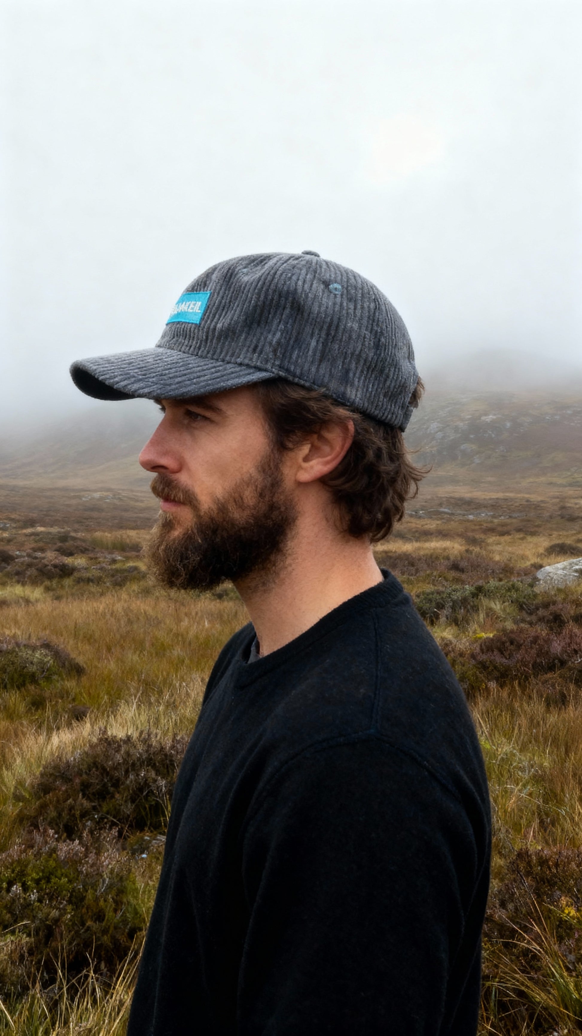 Man wearing a cap with a logo in a misty landscape