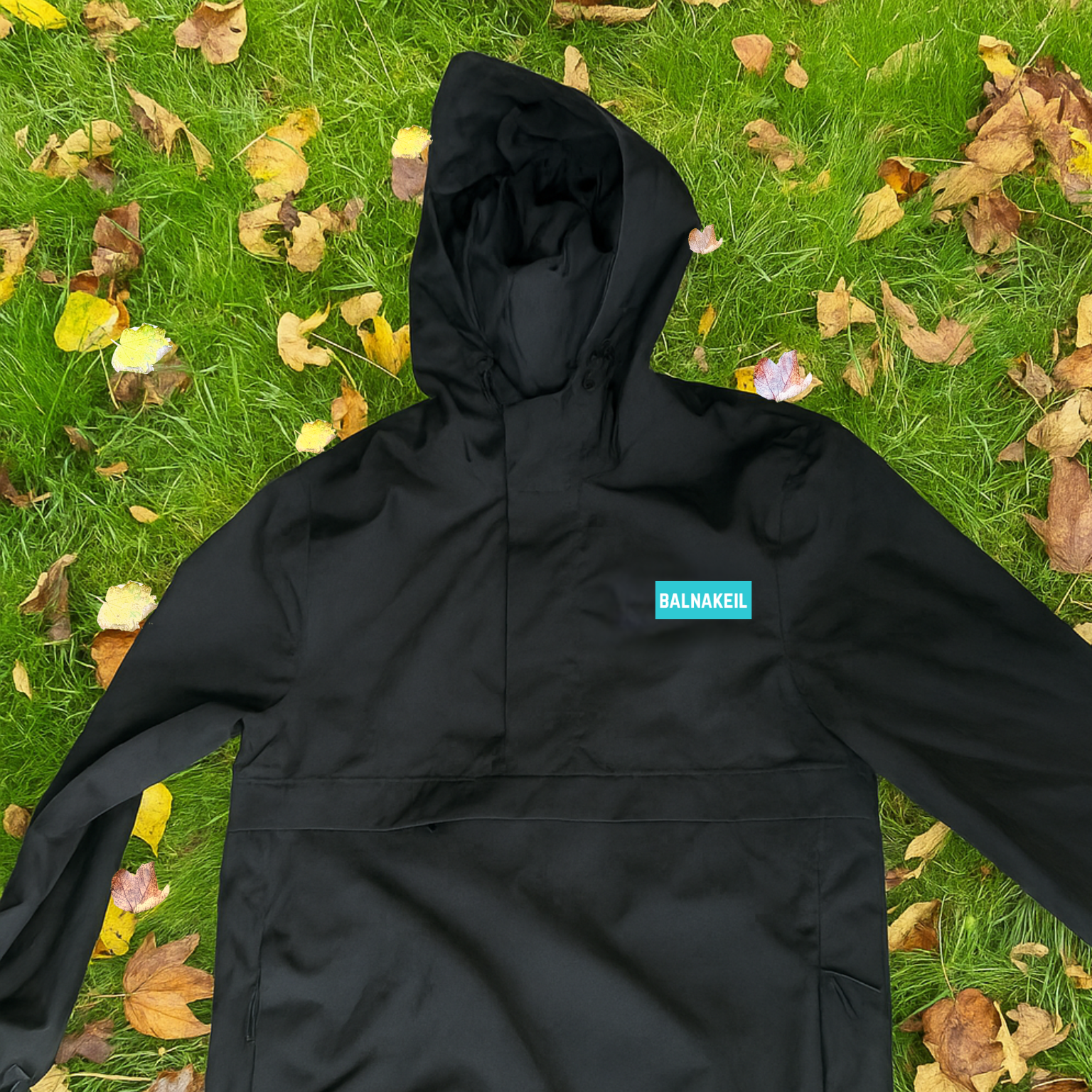 Black hooded jacket with a brand logo on a grassy background with fallen leaves
