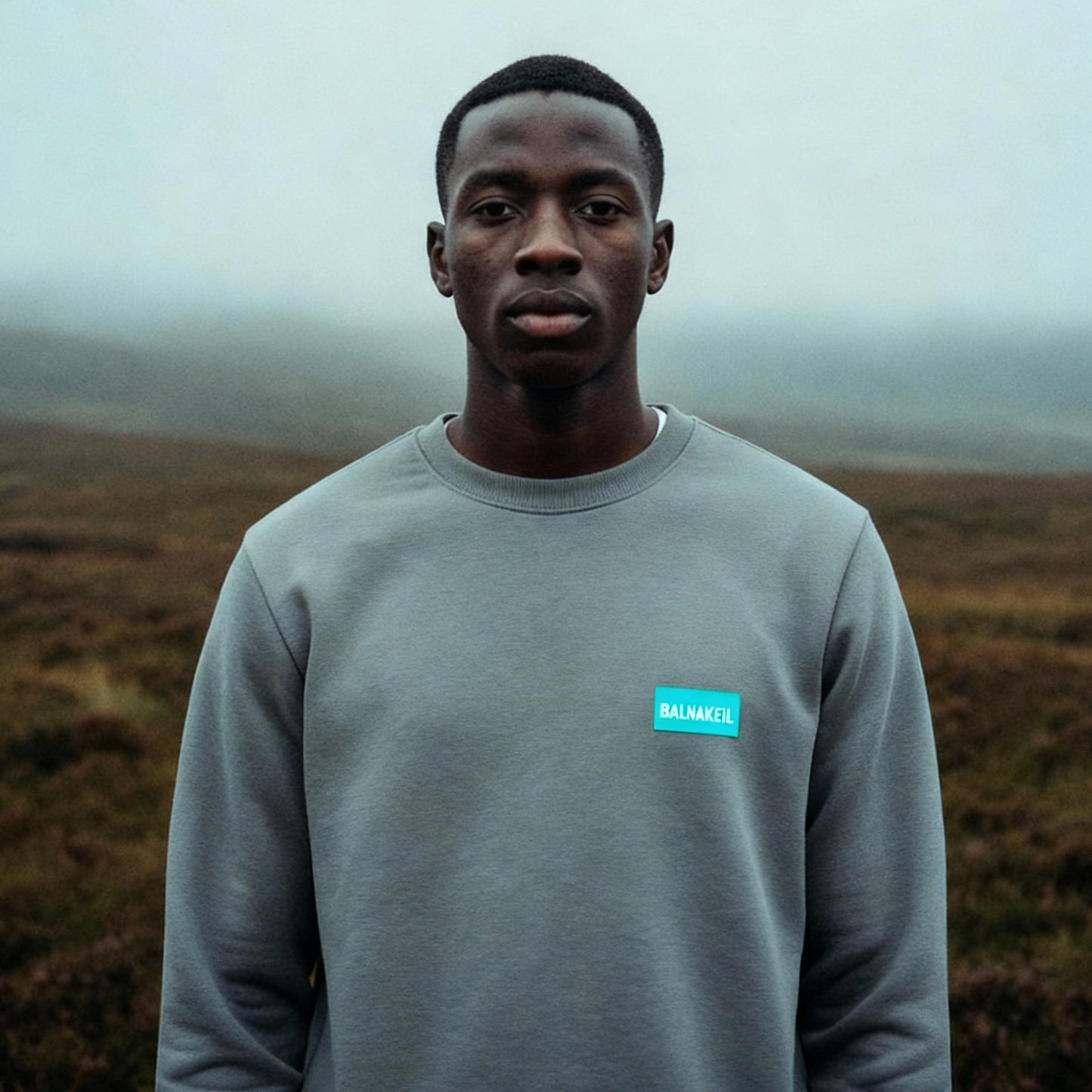 Person wearing a gray sweatshirt with a blue logo in a foggy landscape