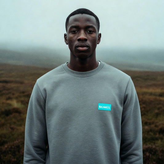 Person wearing a gray sweatshirt with a blue logo in a foggy landscape