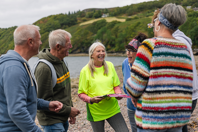 A community group standing by a body of water with green hills in the background