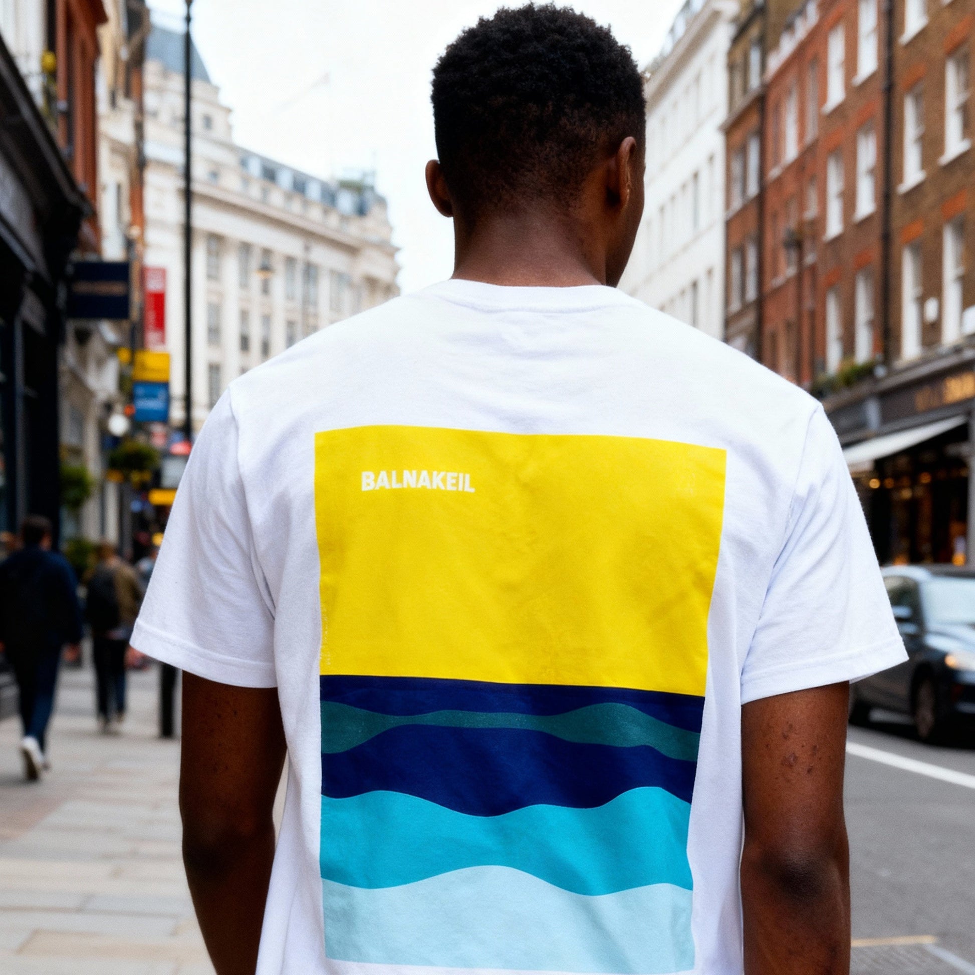 Person wearing a white t-shirt with colorful design on the back in an urban setting