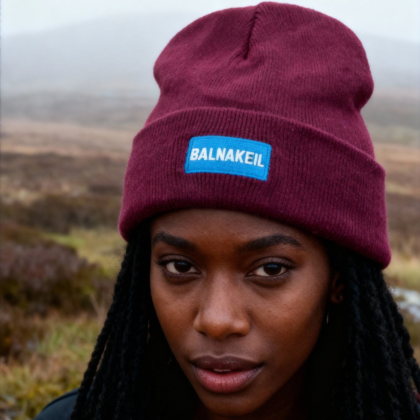 Person wearing a maroon beanie with a blue logo in a natural setting
