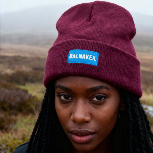 Person wearing a maroon beanie with a blue logo in a natural setting