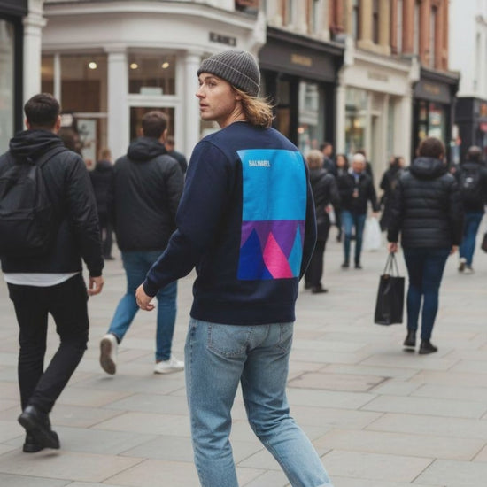 Man in city street wearing a navy blue sweat top with mountain design.