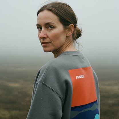 Woman wearing a grey sweatshirt with a colorful design, standing in a misty landscape.